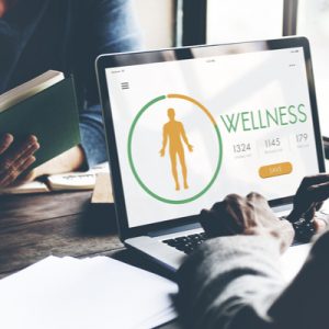 A person sits at a computer. The screen shows a wellness program enrollment page.